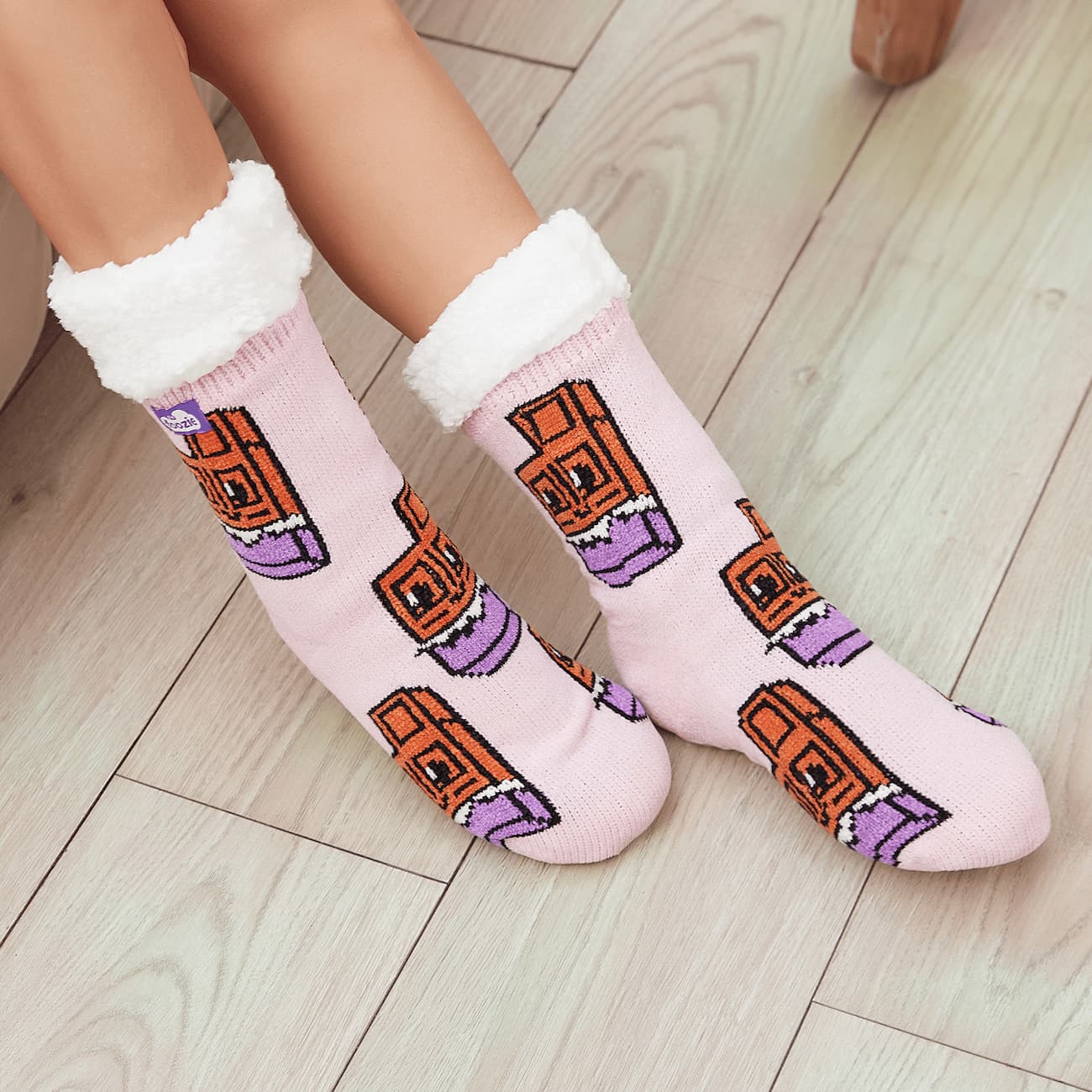 The Foozie™ Chocolate slipper socks, chocolate bar print on pink, worn on a wooden floor