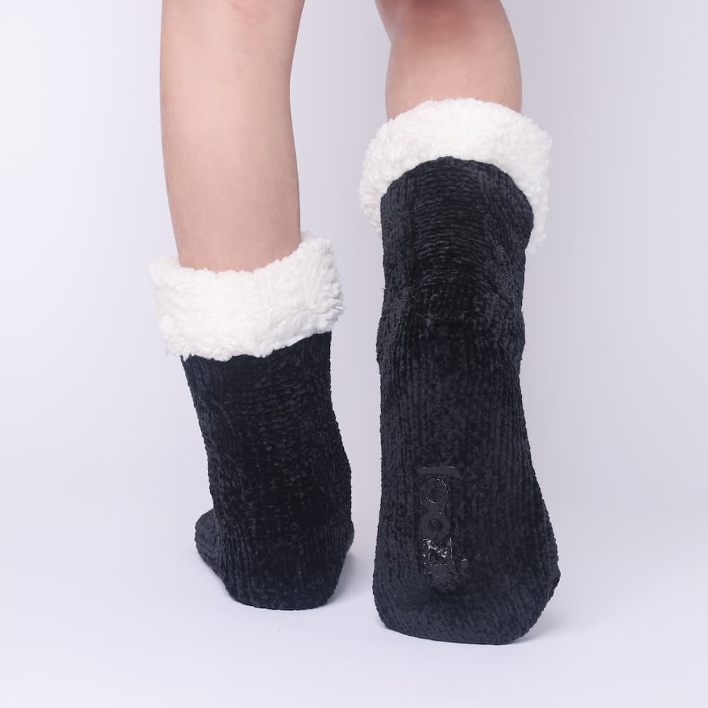 The Foozie™ in Black, back view worn in Kids/Small with one foot raised to show the non-slip grips on the sole